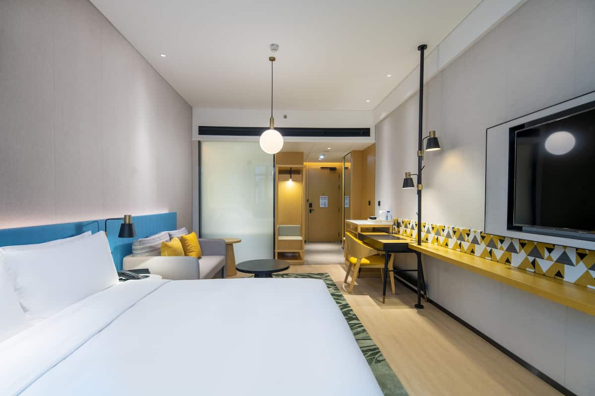 Une chambre d’hôtel moderne équipée d’un grand lit, d’un bureau, d’une chaise, d’un canapé et d’une télévision.