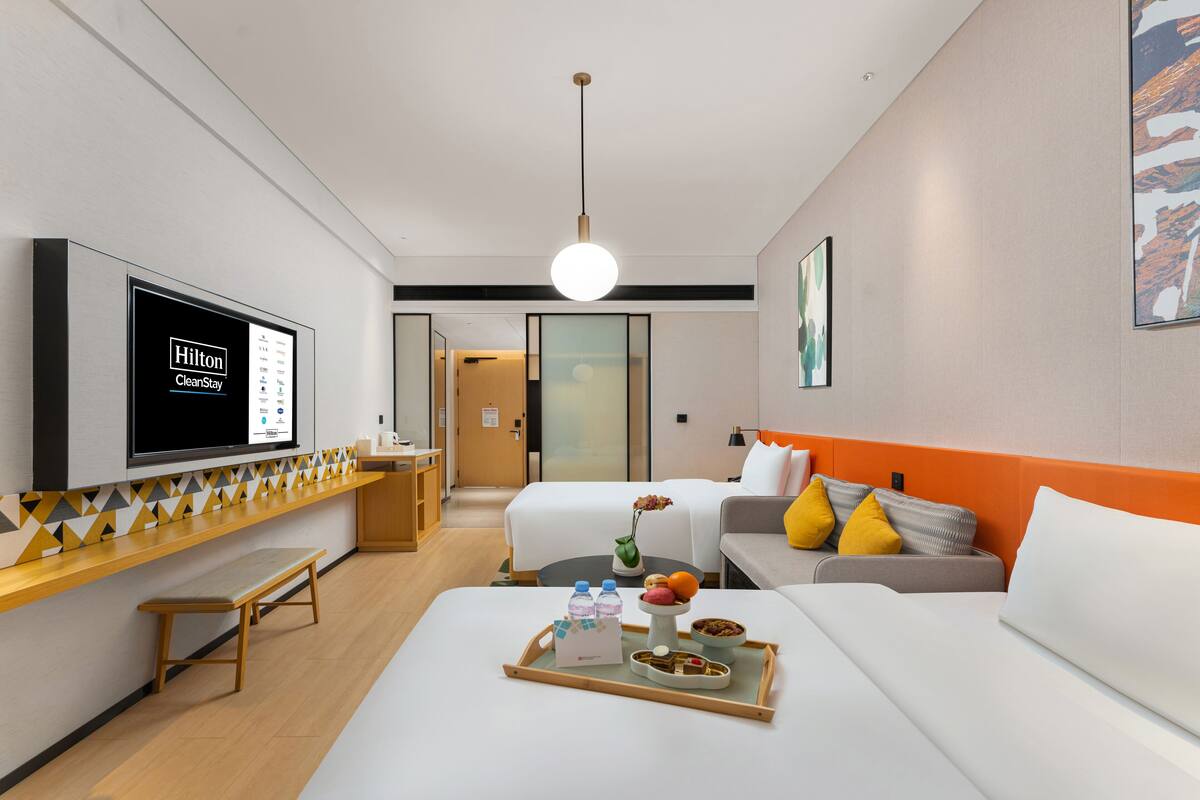 Une chambre d’hôtel moderne équipée d’un lit, d’un canapé, d’une télévision et d’un plateau avec de la nourriture et des boissons.