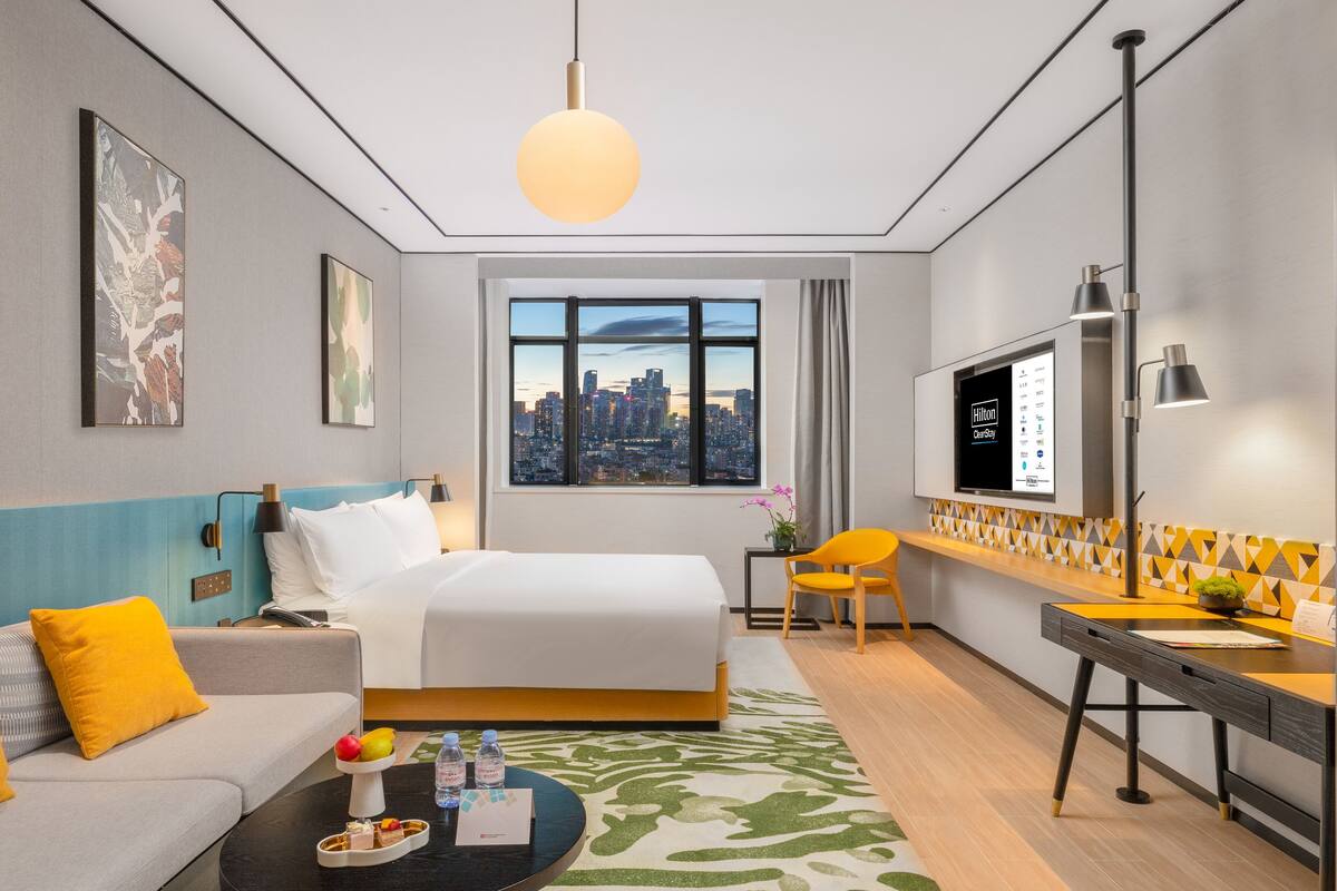 Une chambre d’hôtel avec un lit, un canapé, un bureau, une télévision et une vue sur la ville.