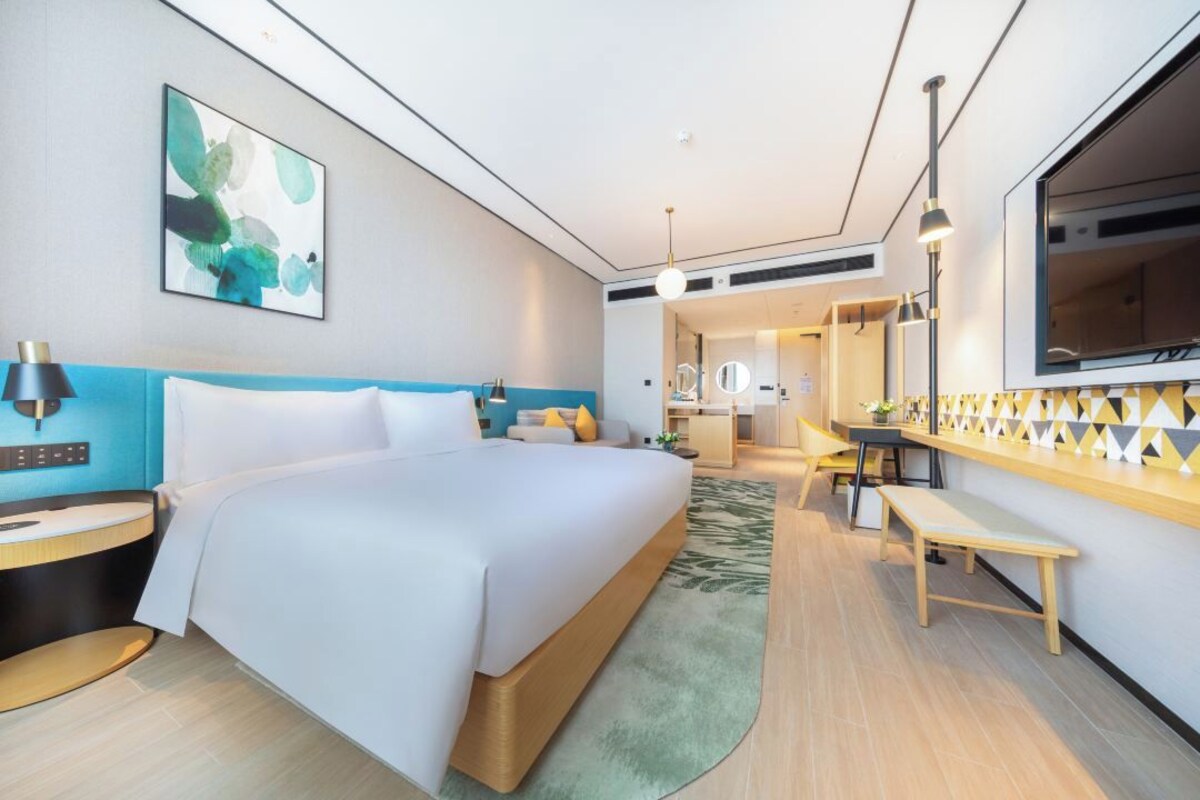A modern hotel room with a large bed, bedside tables, a desk, and a mirror.