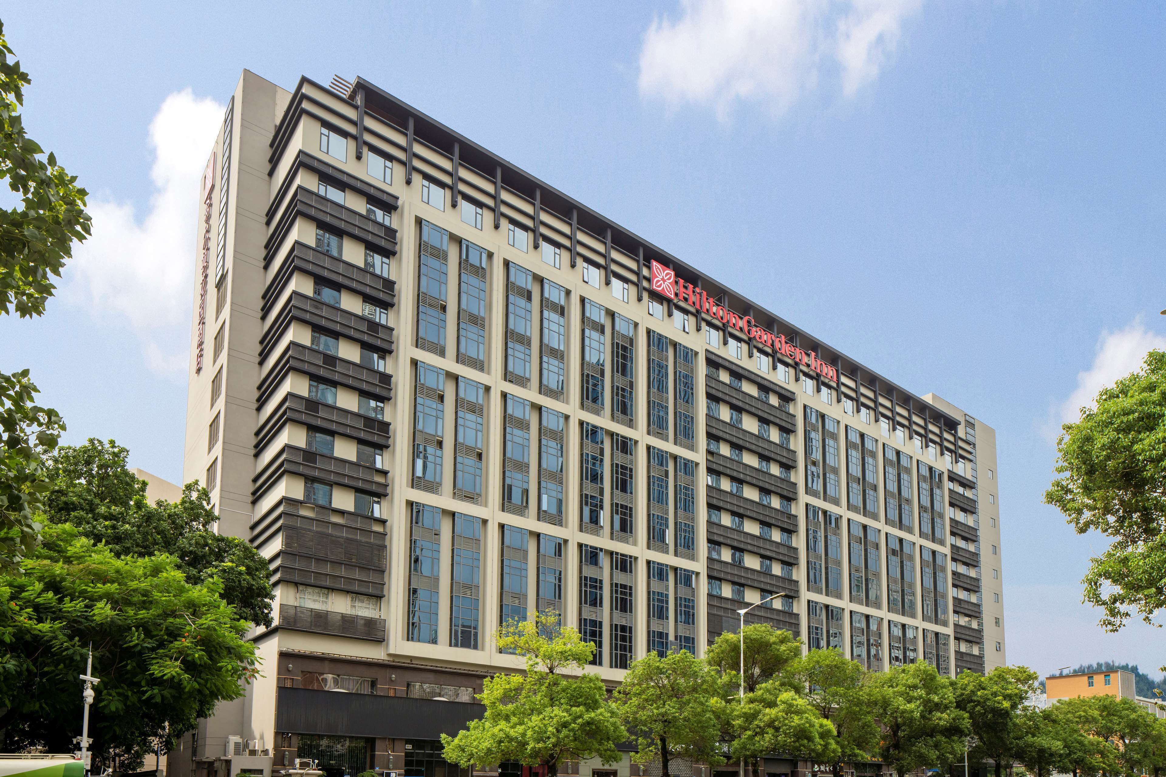 A modern hotel building with multiple floors, large windows, and a prominent Hilton Garden Inn sign.