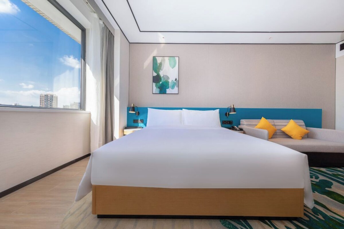 A hotel room with a large bed, a sofa, a painting on the wall, and a view of the city.