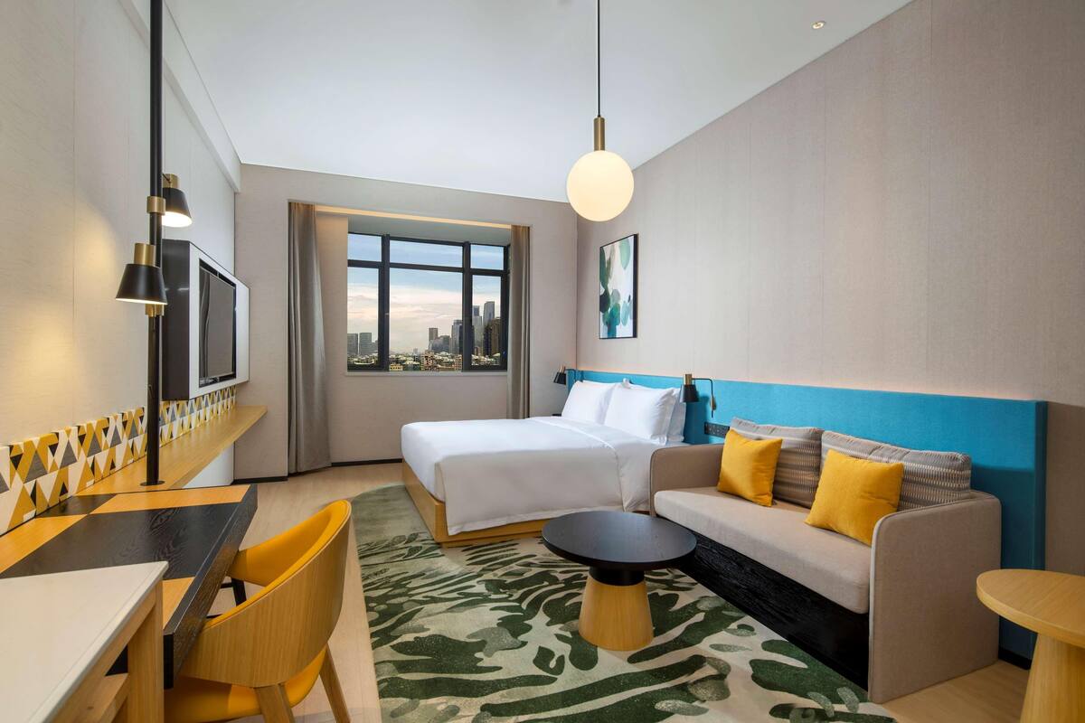 Une chambre d’hôtel équipée d’un lit, d’un canapé, d’une table à manger, de chaises, d’un téléviseur et offrant une vue sur la ville.