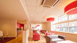 Een modern café met houten vloeren, rode en grijze zitplaatsen en grote ramen met uitzicht over de stad.