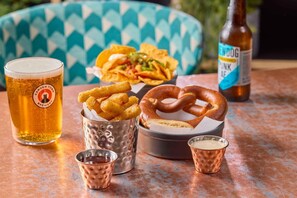 A meal with nachos, pretzel, and fries, a beer glass, and a beer bottle on a table. - Travelodge Derby Pride Park (Derby)