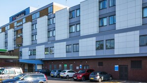 A Travelodge hotel with a modern facade, multiple parking spaces, and a clear blue sky. - Travelodge Luton (Luton)