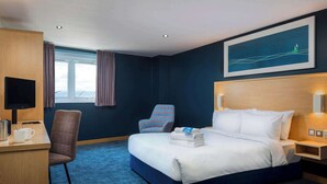A hotel room with a bed, a desk with a TV, a chair, and a window with curtains. - Travelodge Luton (Luton)
