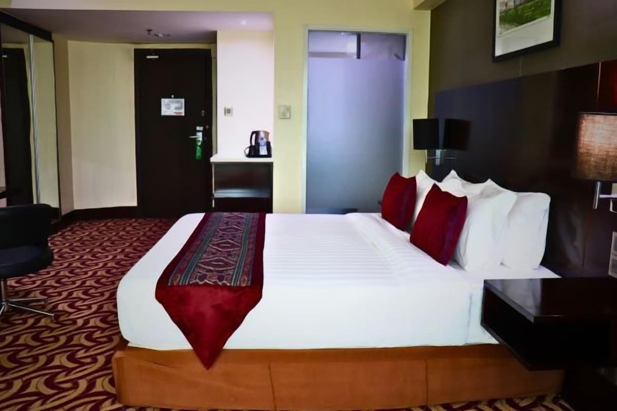 A hotel room with a large bed, a desk, a chair, and a television.