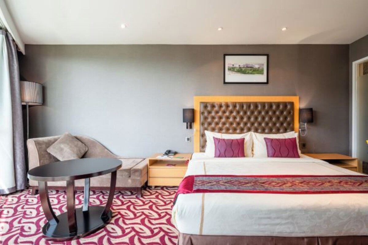 A hotel room with a large bed, a round table, a sofa, and a wall-mounted TV.