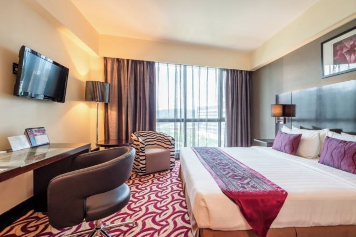 A hotel room with a bed, a desk, a chair, a TV, and a window with curtains.