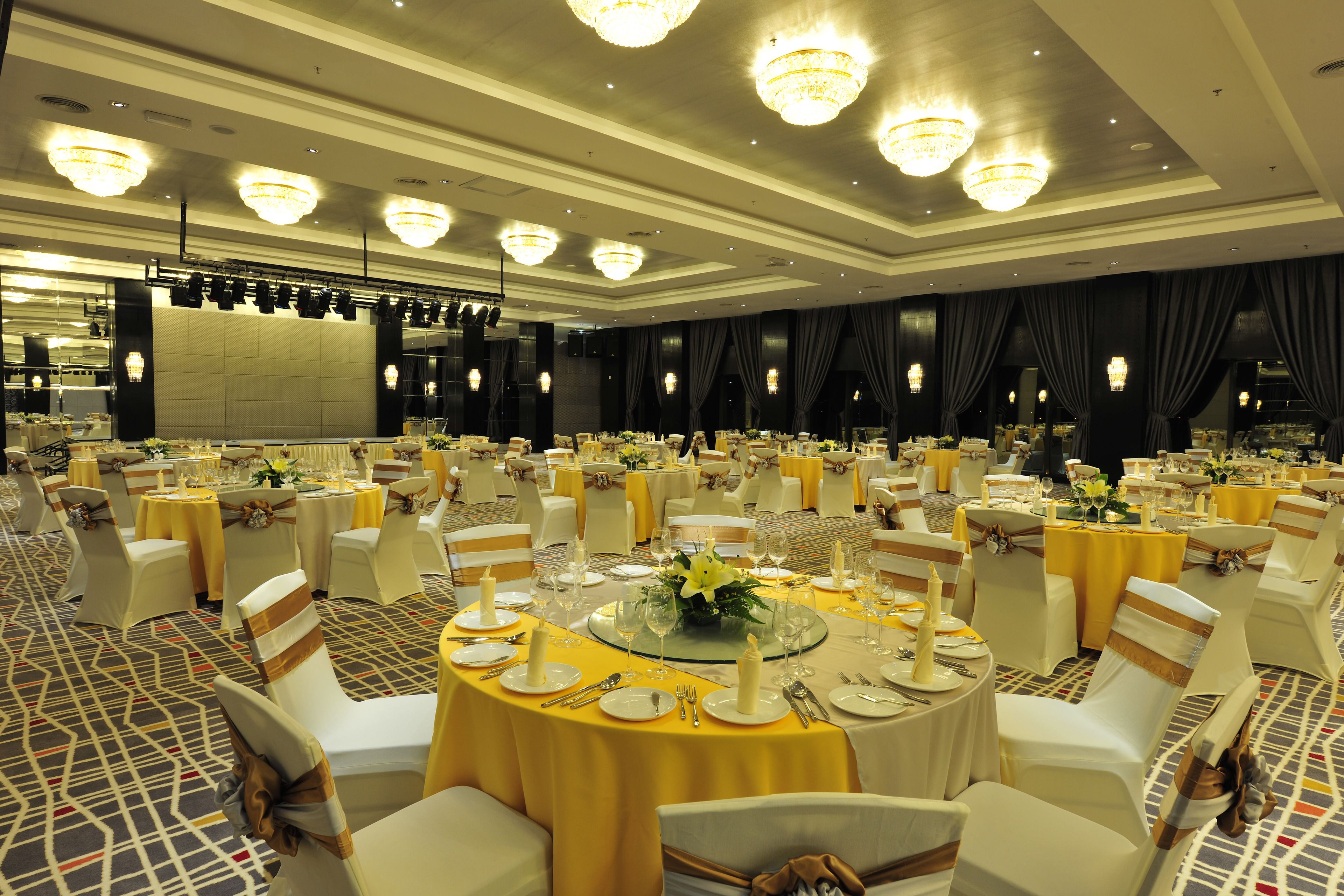 A banquet hall with round tables, white chairs, and chandeliers.