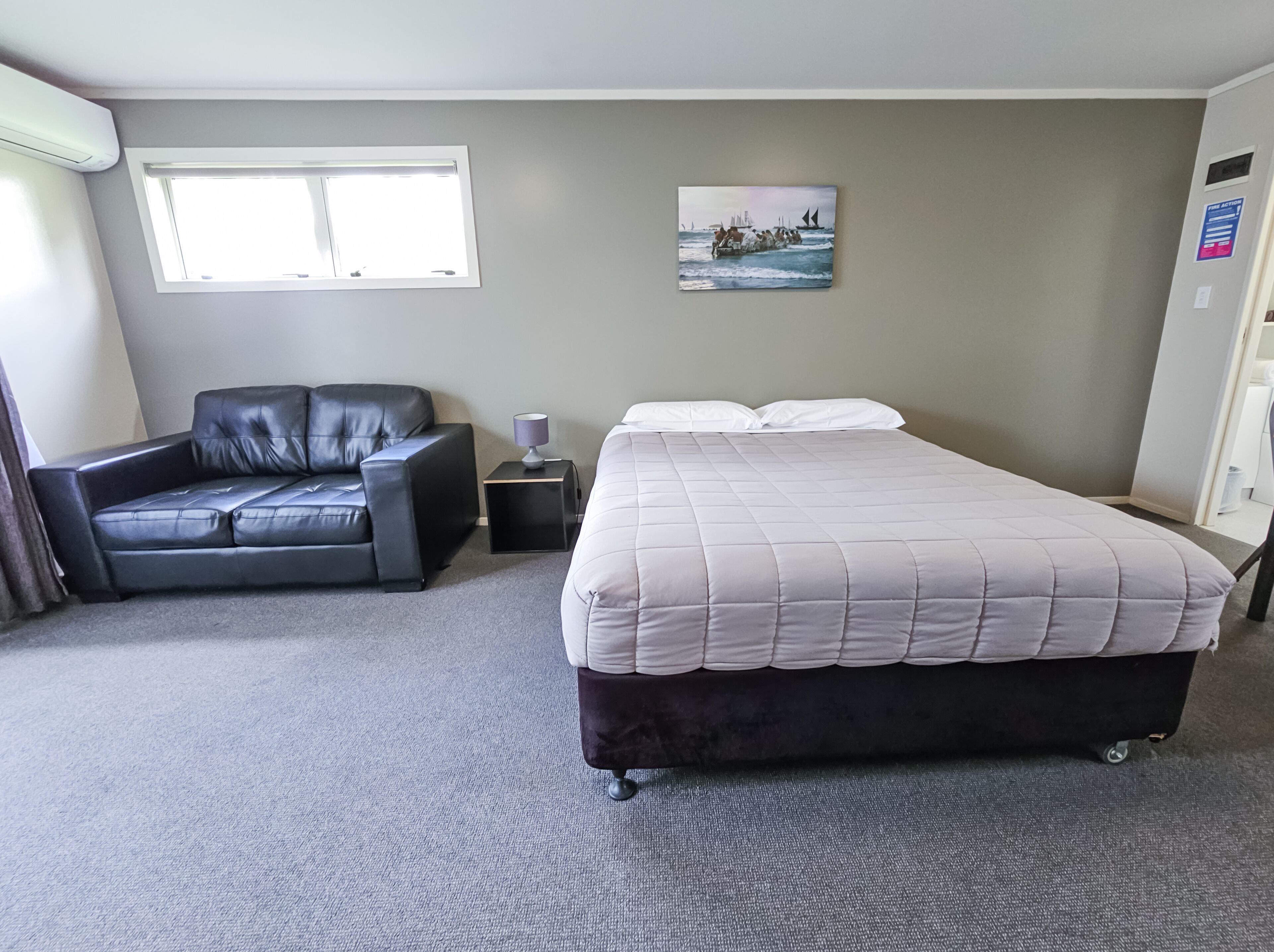 A hotel room with a bed, a sofa, a window, and a painting on the wall.