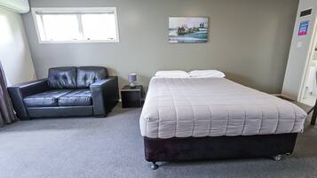 A hotel room with a bed, a sofa, a window, and a painting on the wall.