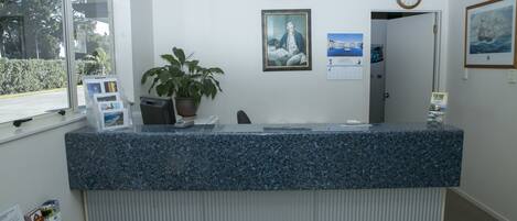 Una mesa de recepción con cubierta de granito azul, una planta en maceta, cuadros en la pared y un reloj.