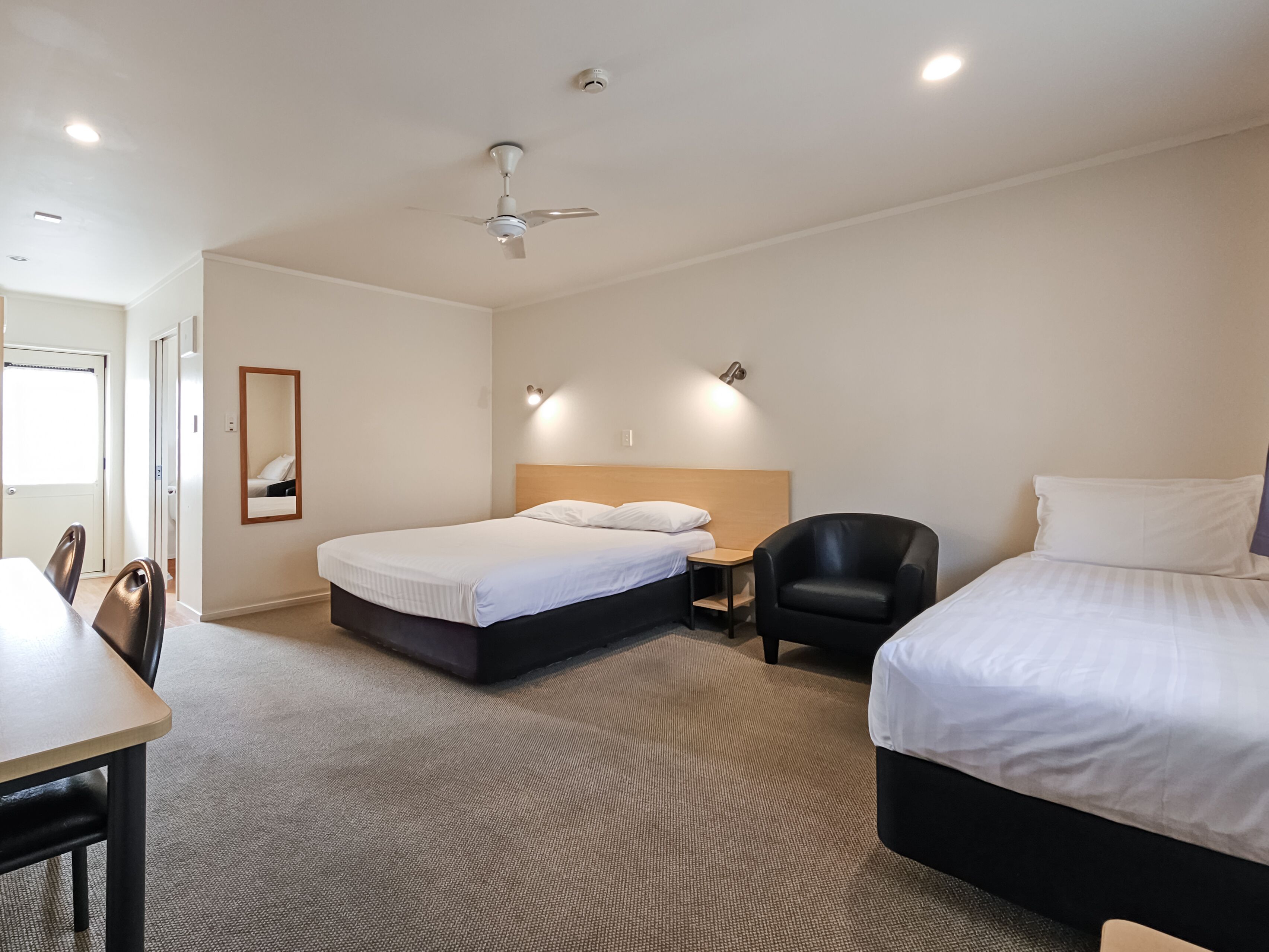 A hotel room with a bed, a desk, a chair, a ceiling fan, and a mirror.