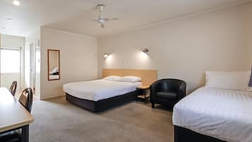 Quarto de hotel com cama, escrivaninha, cadeira, ventoinha no teto e espelho.