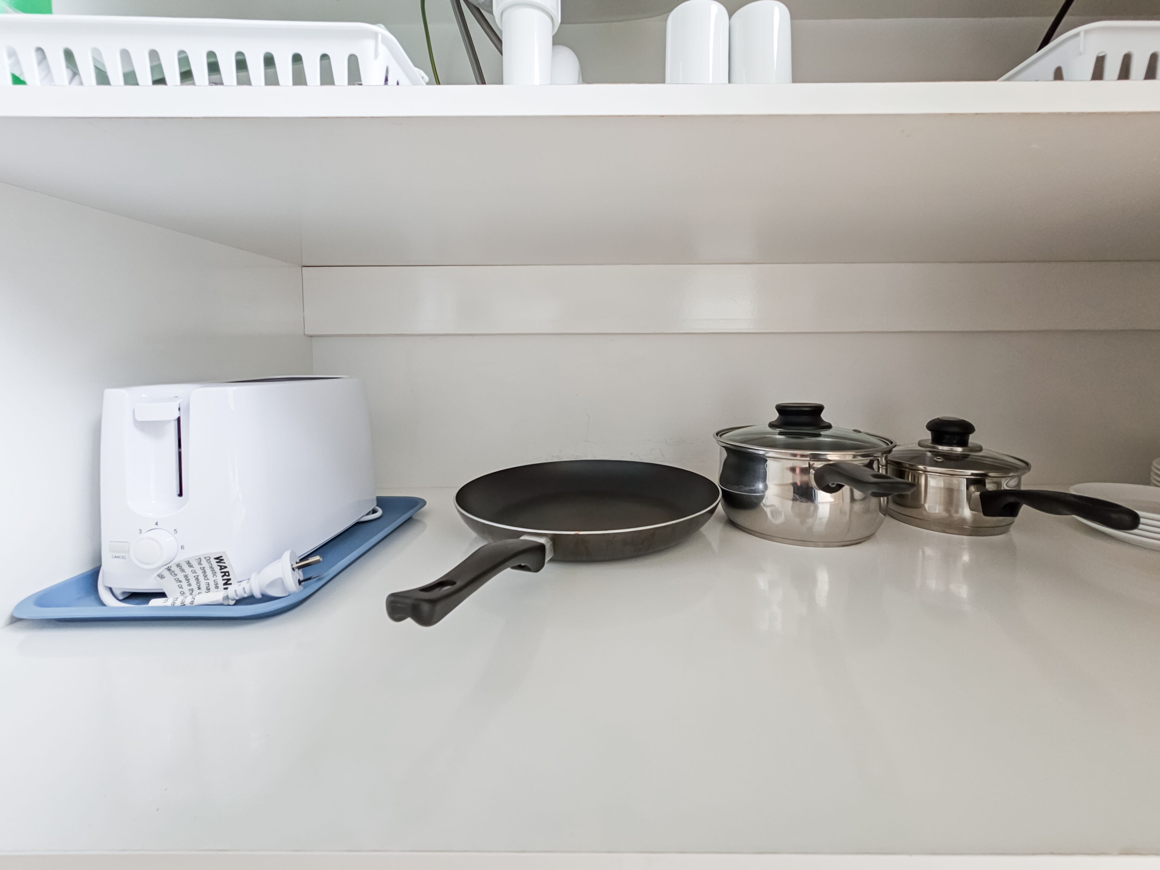 A kitchen with a toaster, a frying pan, and two pots on a white countertop.