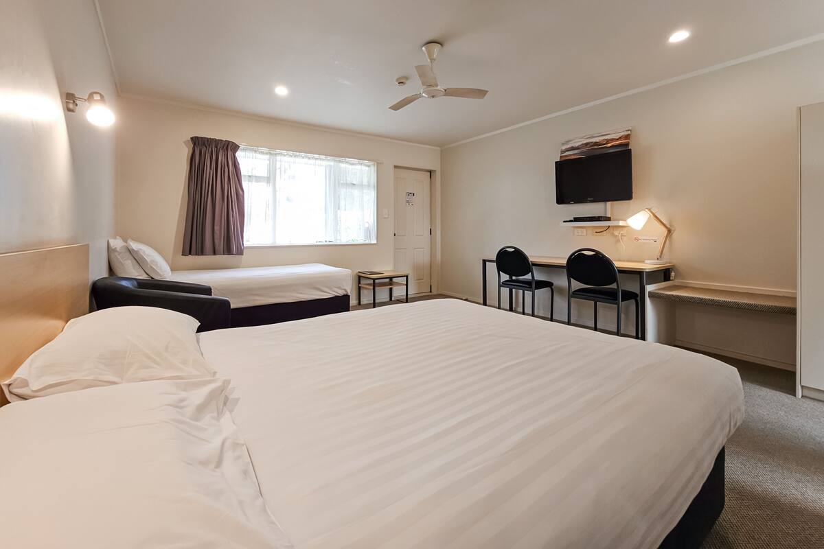 A hotel room with two beds, a desk with a chair, a TV, and a ceiling fan.