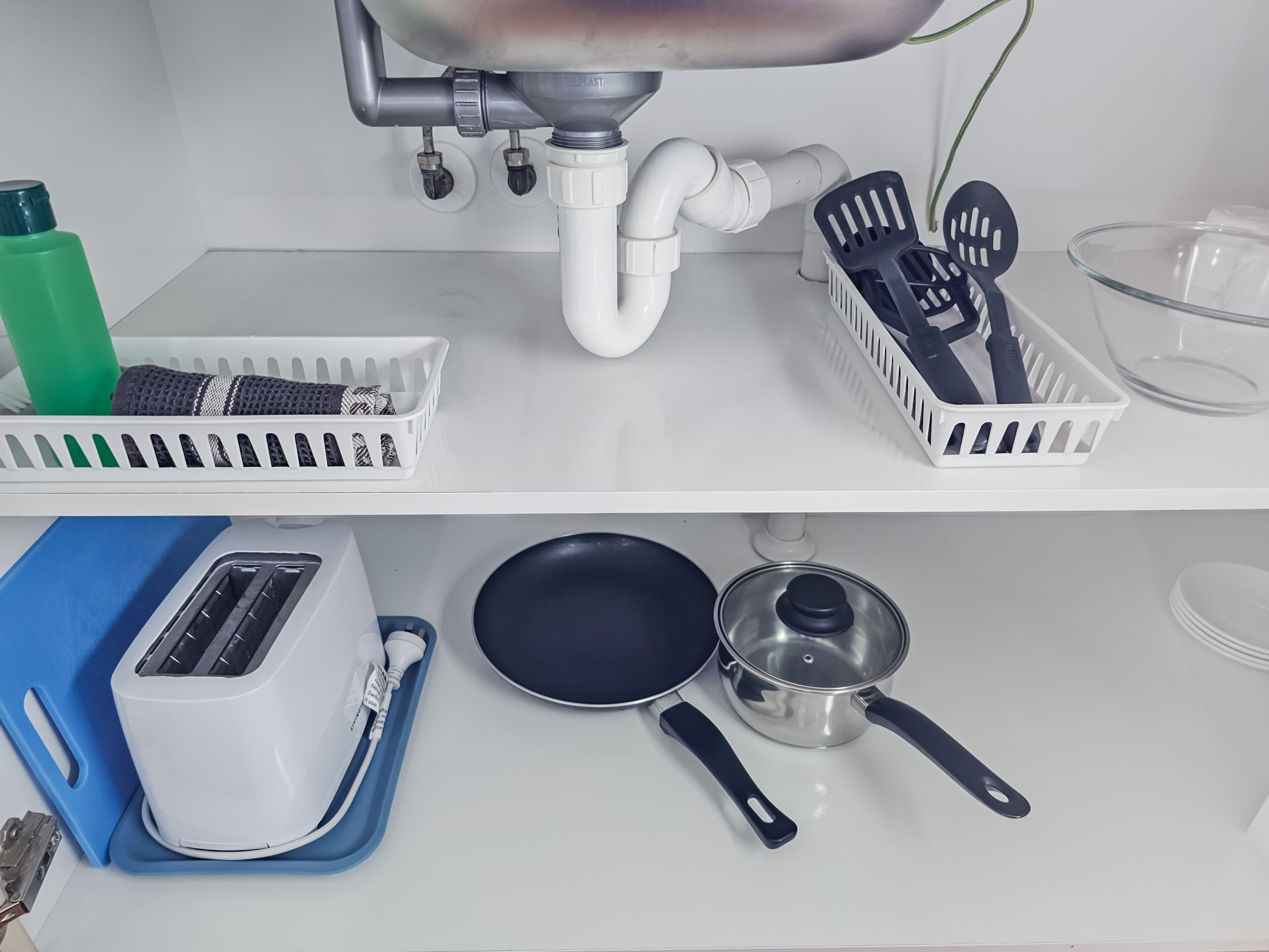 A kitchen with a white countertop, a toaster, a frying pan, a pot, and kitchen utensils on shelves.