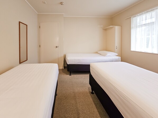 A hotel room with two single beds, a door, a window with sheer curtains, and a small mirror on the wall. - Captain Cook Motor Lodge (Gisborne)