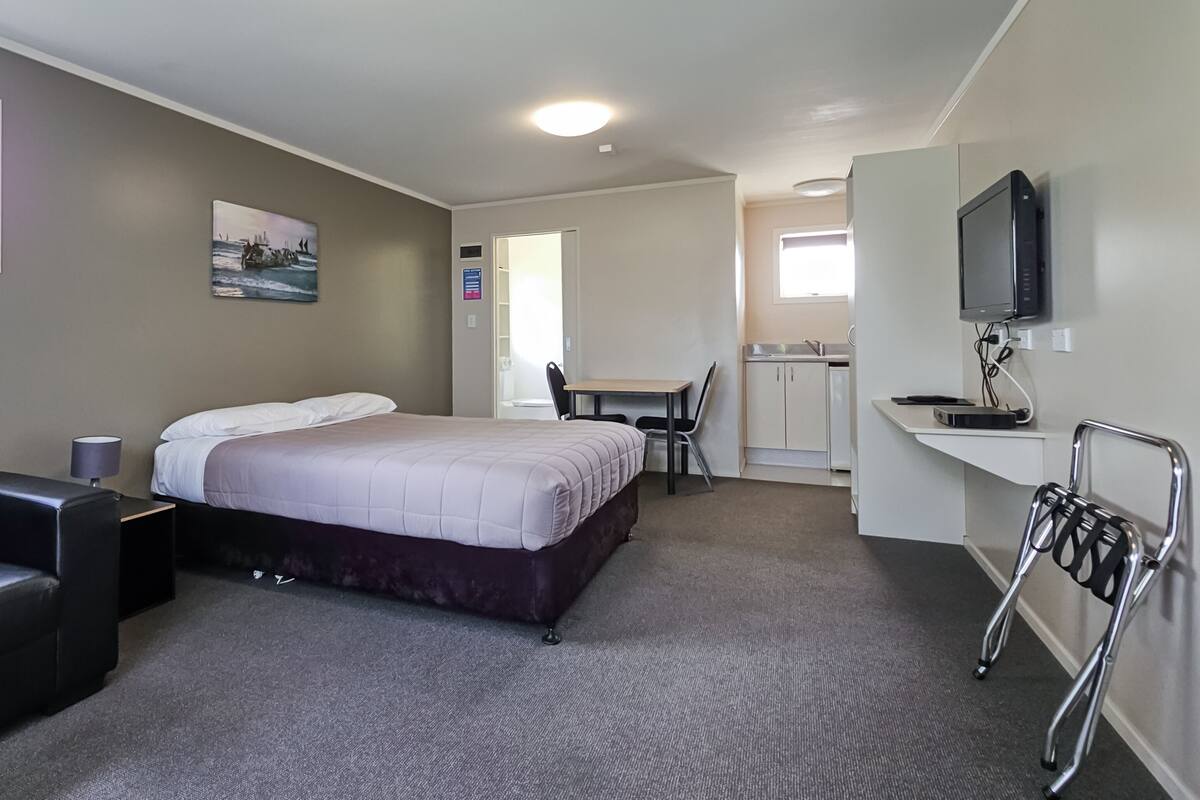 A hotel room with a bed, a desk, a chair, a TV, and a wheelchair.