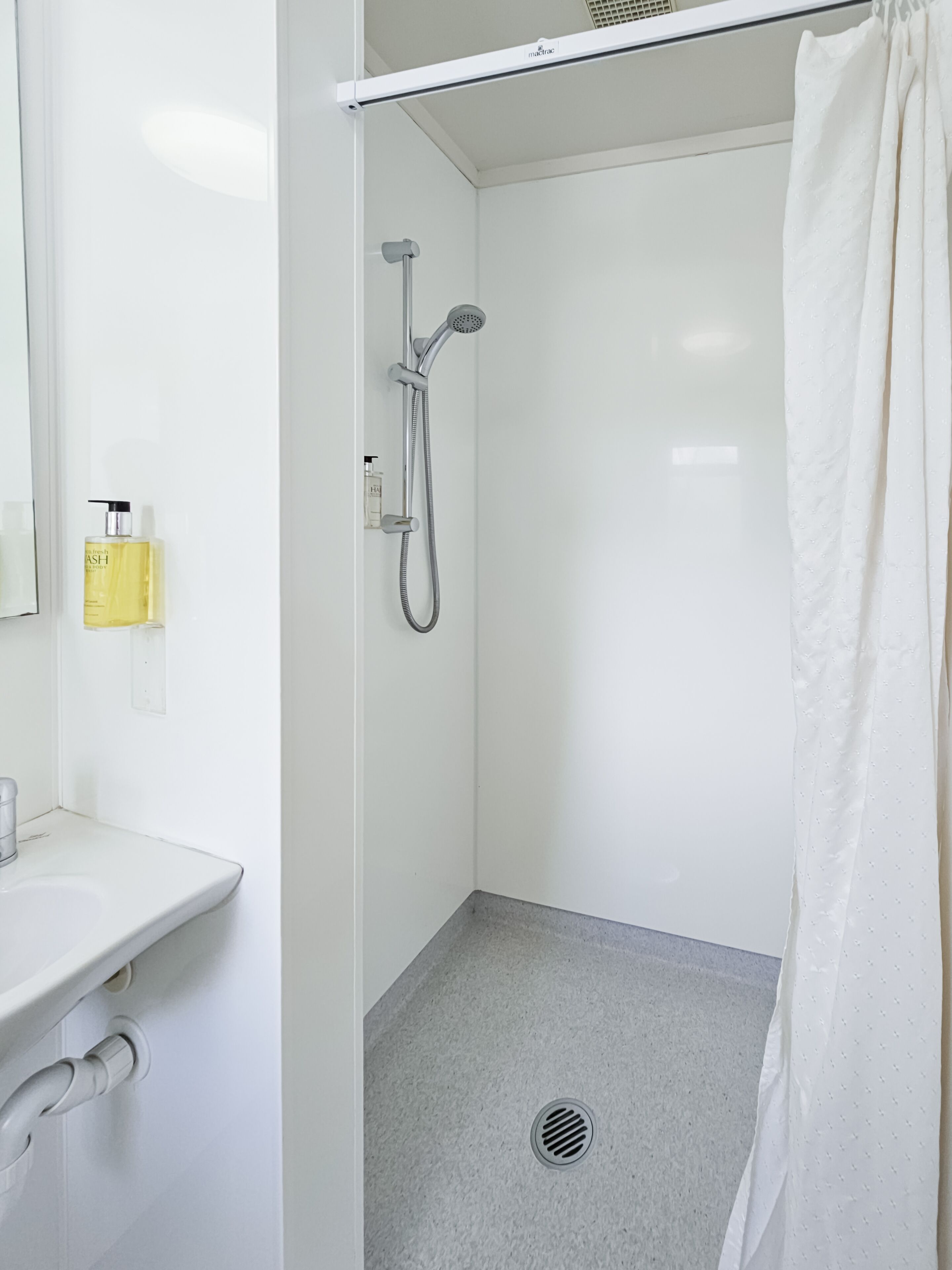 A small, white bathroom with a shower, a sink, and a mirror.