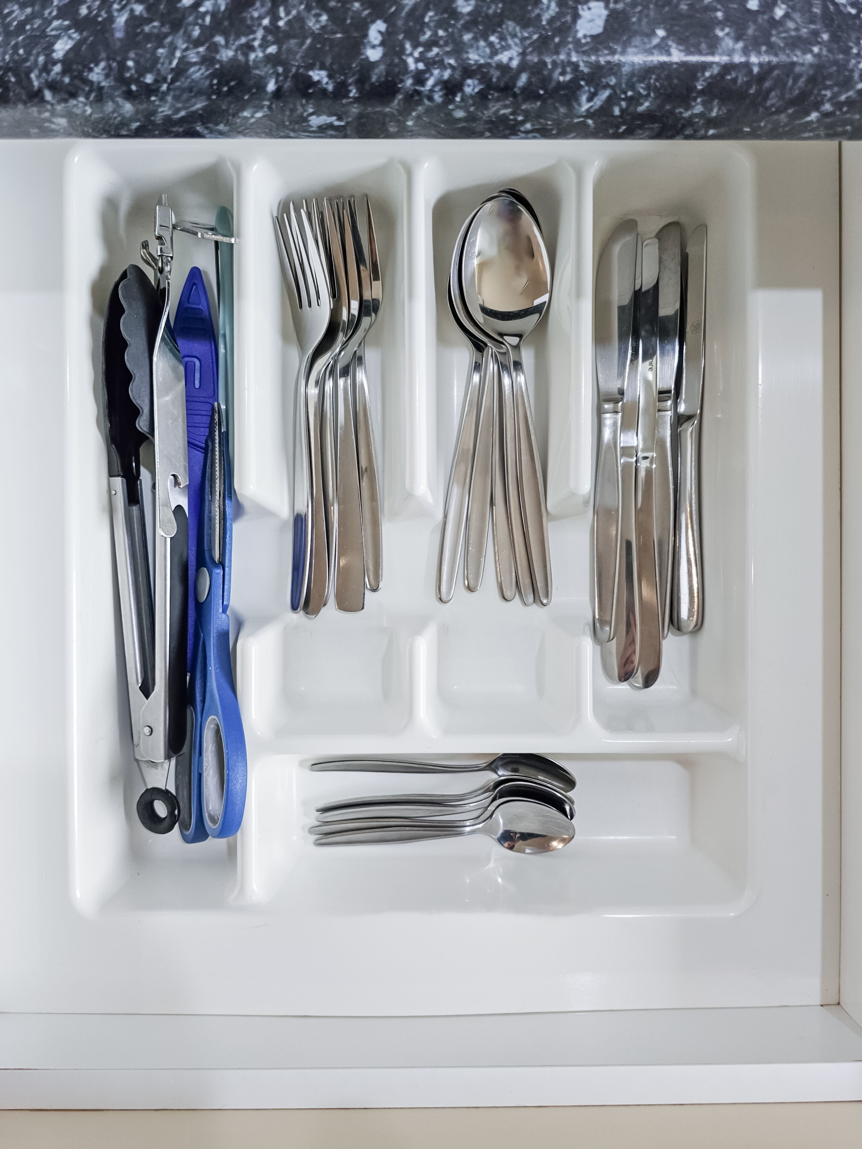 A drawer with utensils and tools, including a knife, spoon, fork, and scissors.