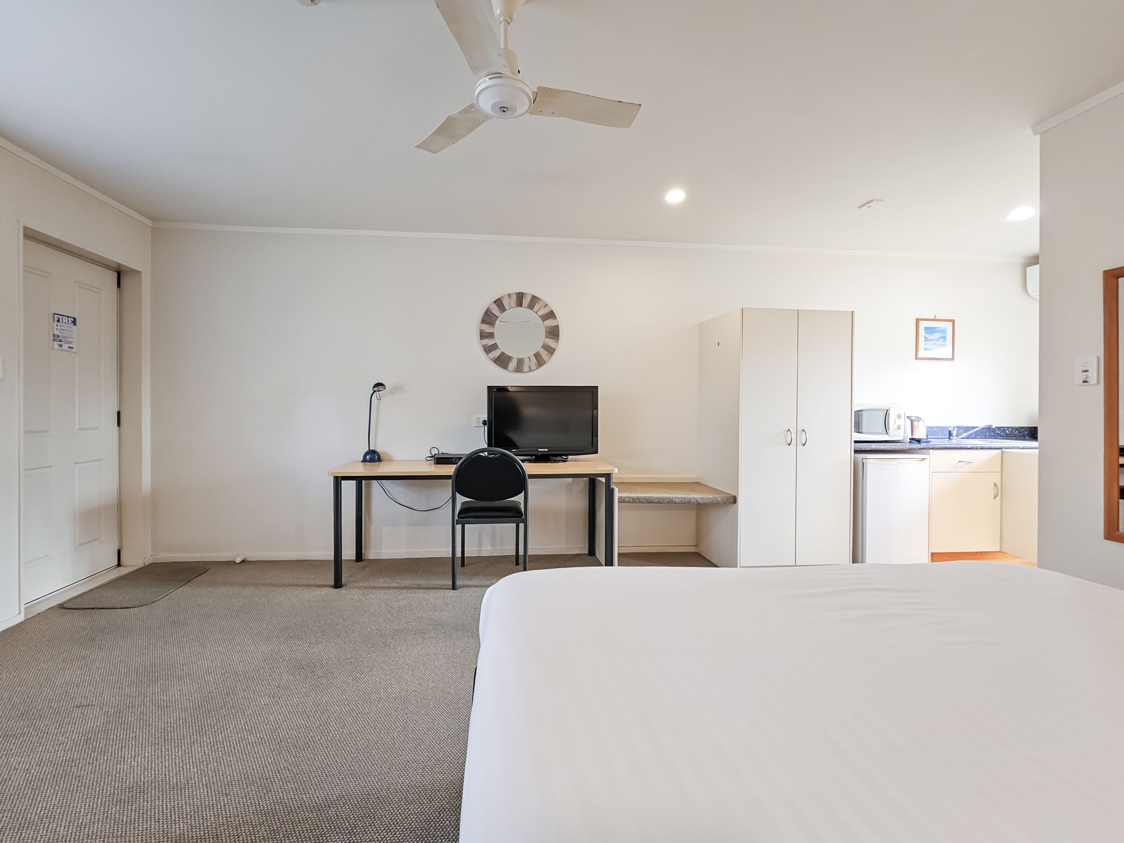 A hotel room with a bed, a desk with a computer, a chair, a wardrobe, and a kitchenette.