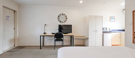 Una habitación de hotel con una cama, un escritorio con computadora, una silla, armario y kitchenette.