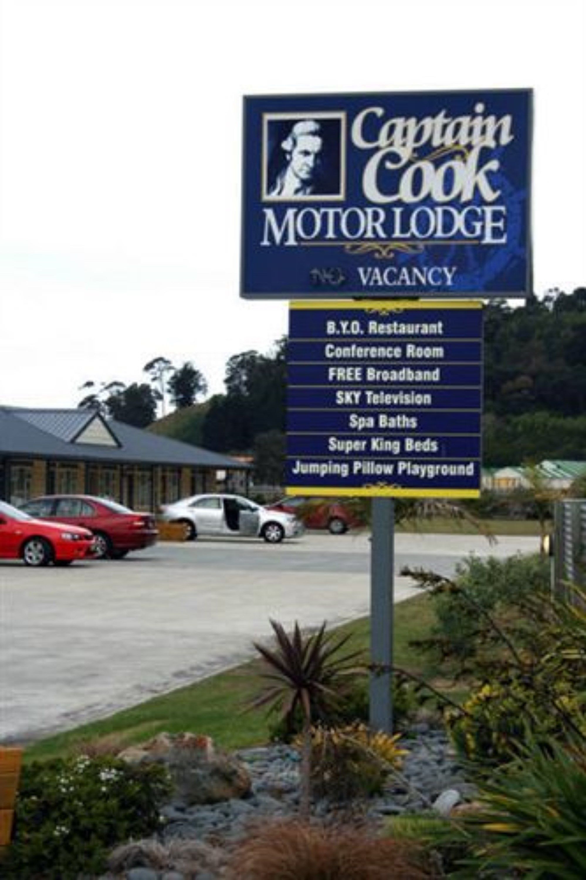 A sign for Captain Cook Motor Lodge advertising amenities such as a B.Y.O. Restaurant, conference room, free broadband, SKY television, spa baths, super king beds, and a jumping pillow playground.