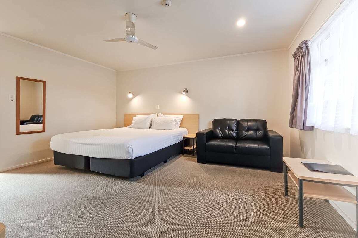A hotel room with a bed, a black leather sofa, a small table, and a ceiling fan.