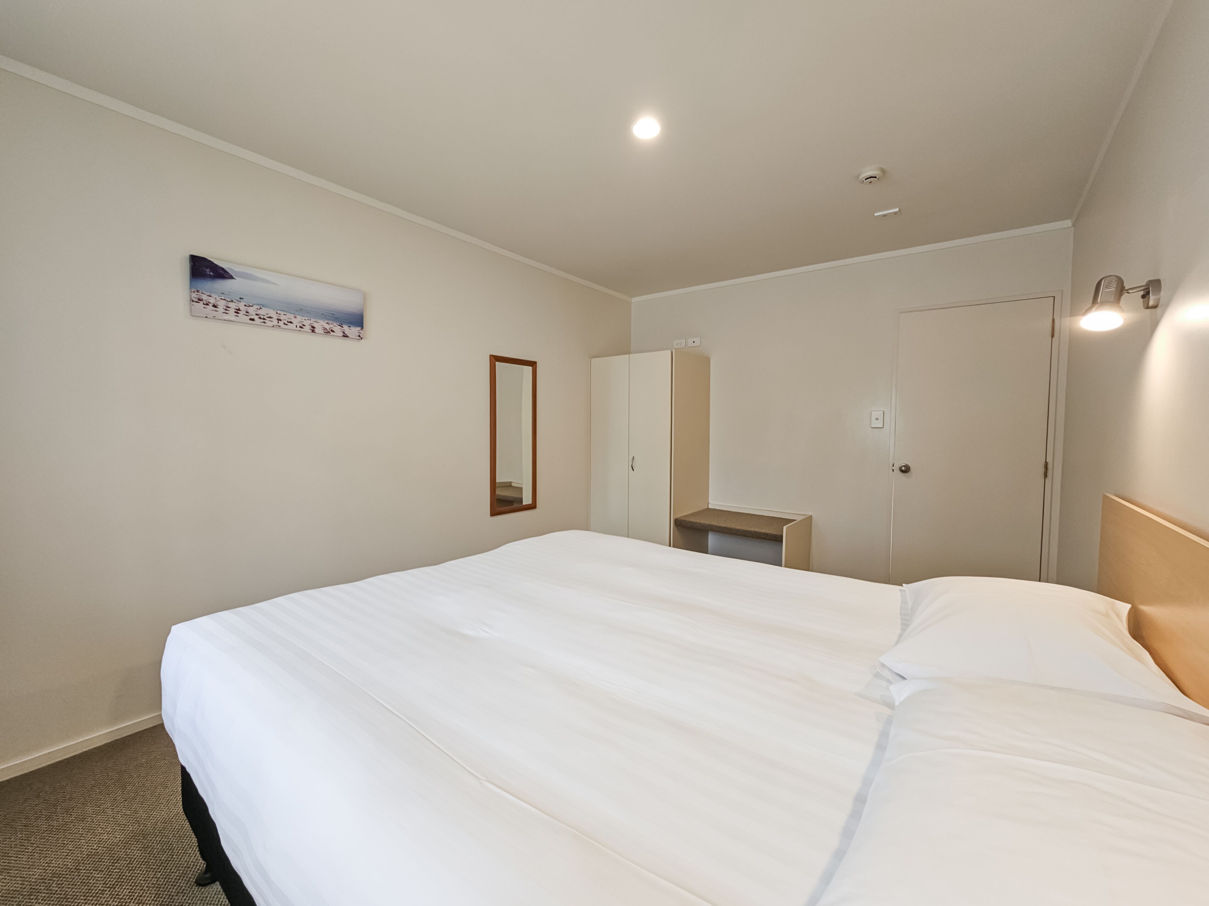 Habitación de hotel con una cama grande, un espejo, un armario, una mesita y un cuadro en la pared.