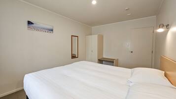 Quarto de hotel com uma cama grande, um espelho, um guarda-roupa, uma mesa pequena e um quadro na parede.