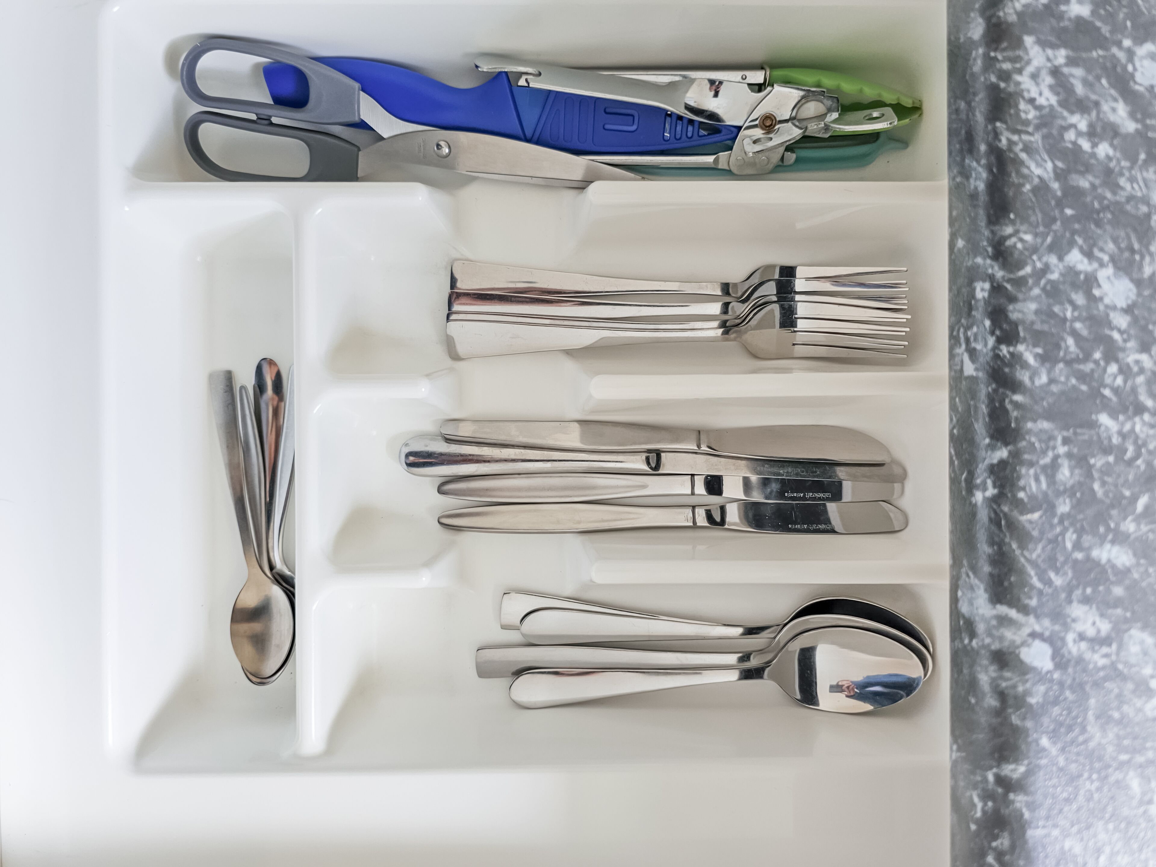 Un cajón con distintos utensilios, incluyendo un par de tijeras, un cuchillo y varias tenedores y cucharas.