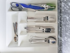 Un cajón con distintos utensilios, incluyendo un par de tijeras, un cuchillo y varias tenedores y cucharas.