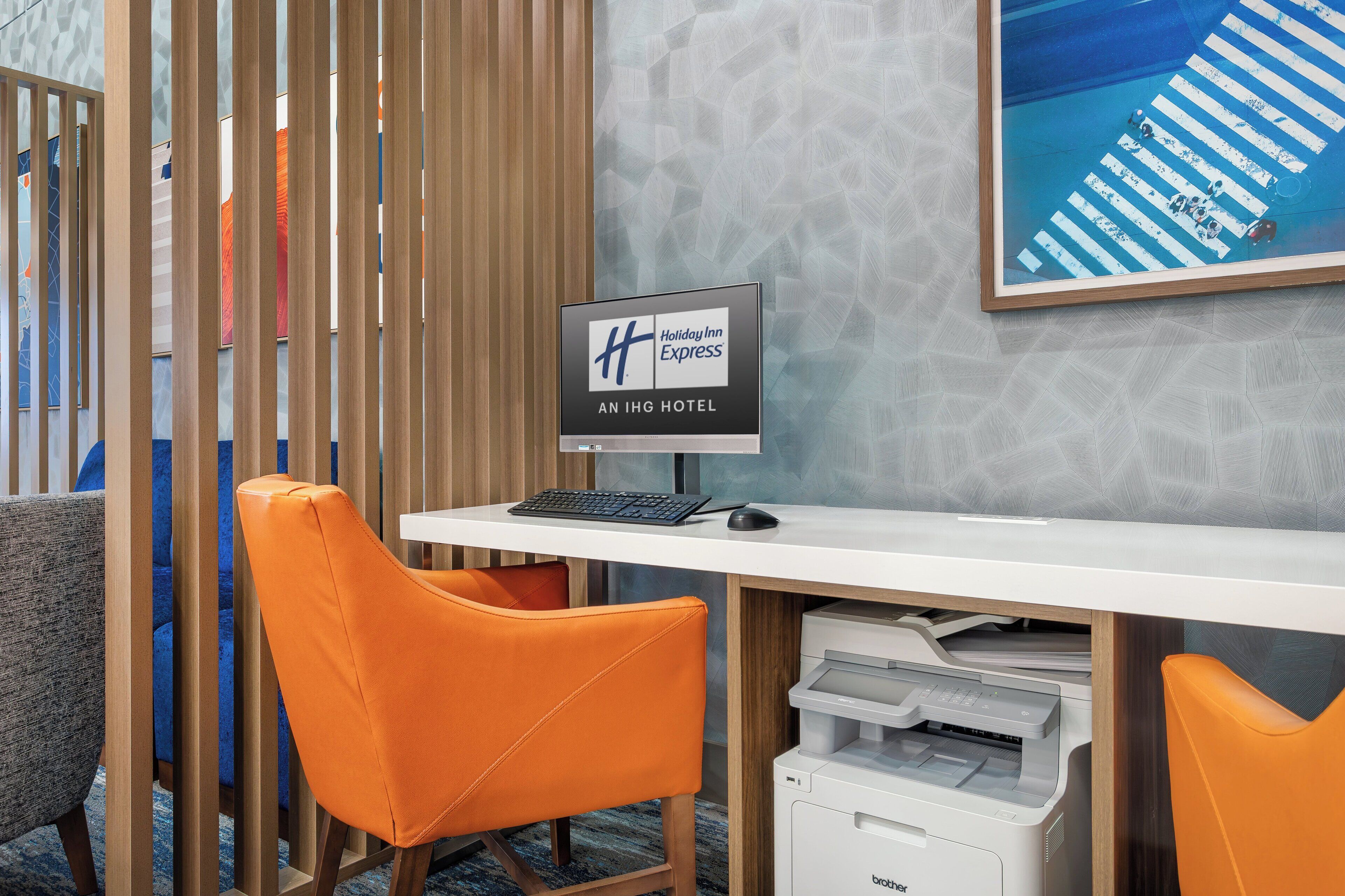 A hotel reception desk with a Holiday Inn Express sign, a computer, a printer, and orange chairs.
