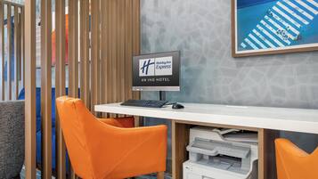 A hotel reception desk with a Holiday Inn Express sign, a computer, a printer, and orange chairs.