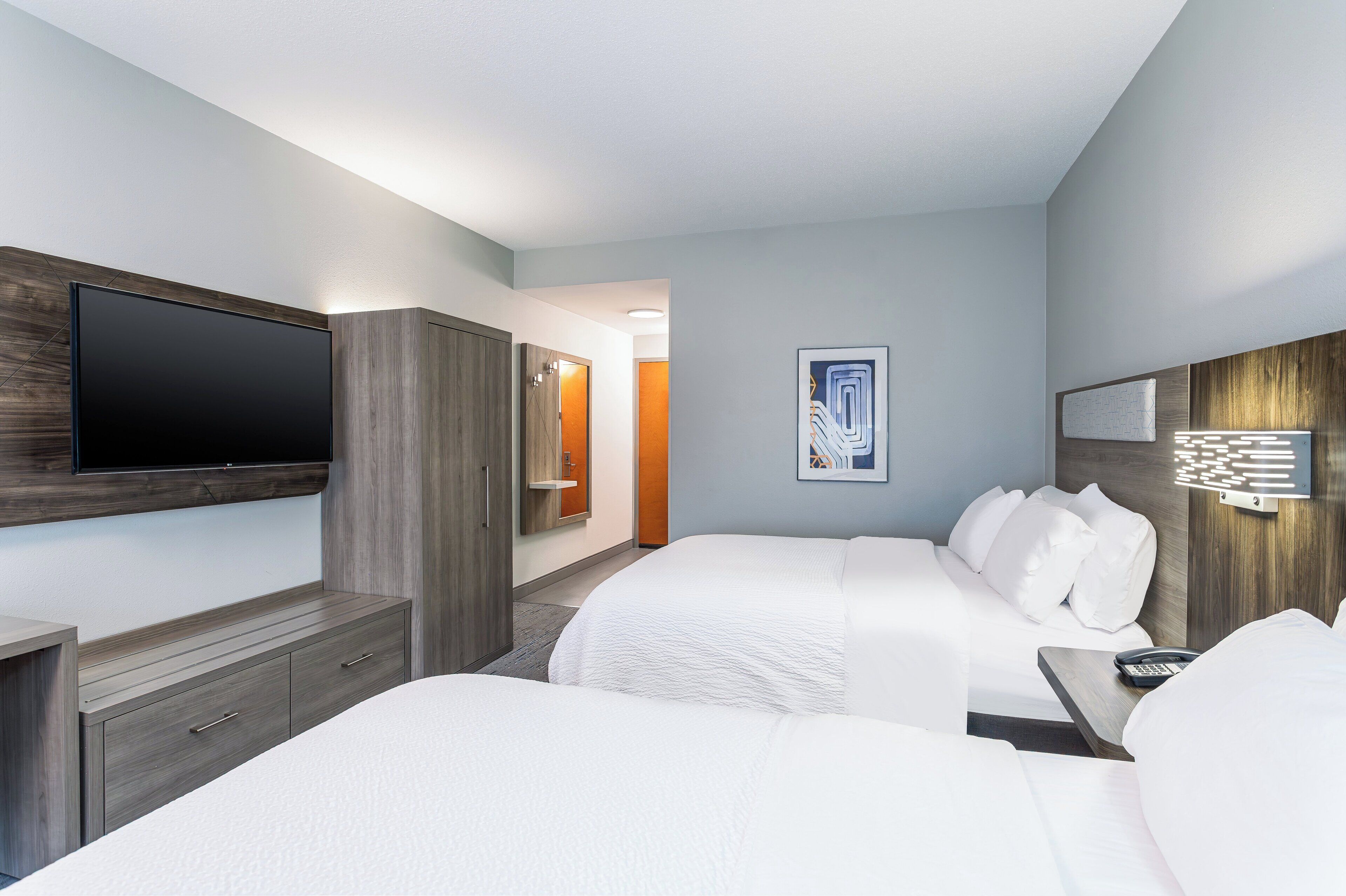A hotel room with two beds, a TV, a desk, and a bathroom visible through an open door.
