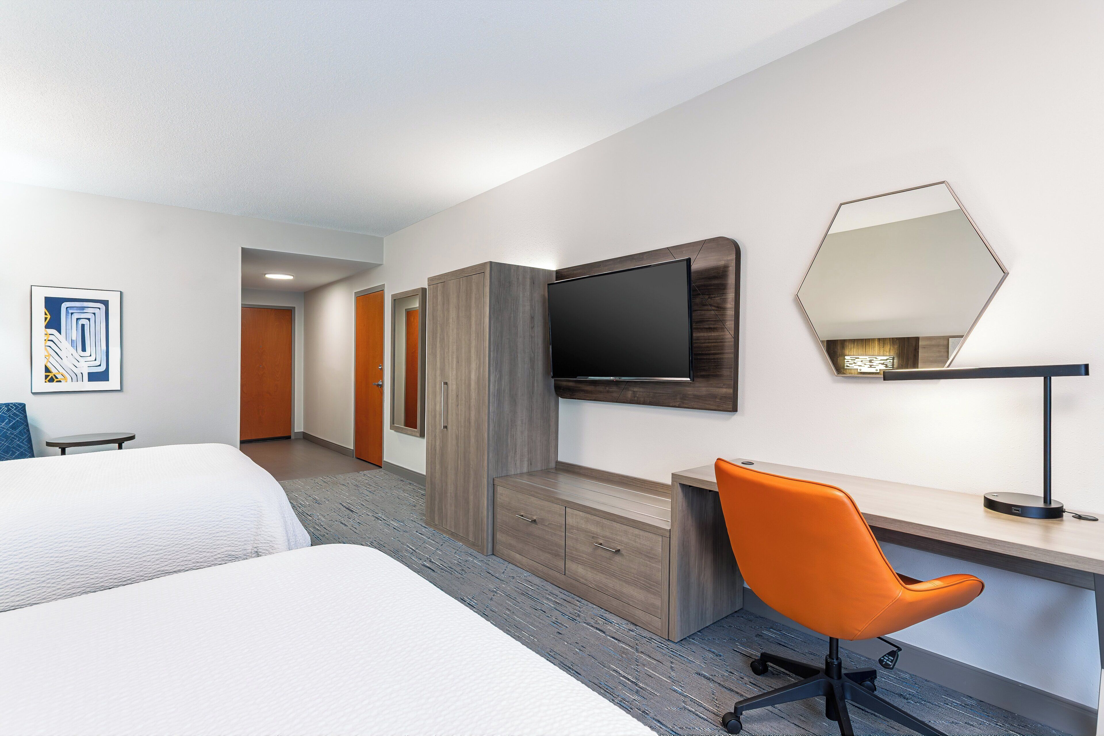 A hotel room with two beds, a desk, a chair, a TV, and a mirror.