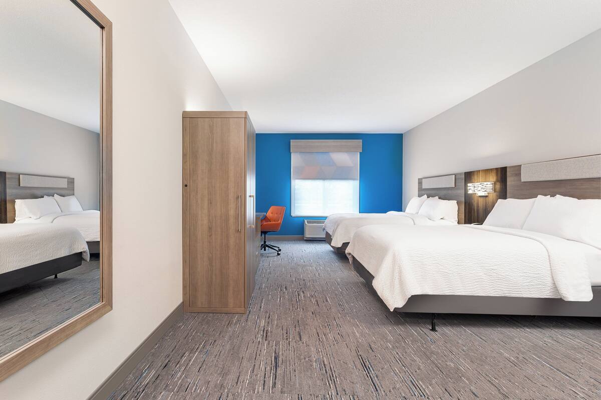 A hotel room with two beds, a wardrobe, a desk, and a window with blinds.