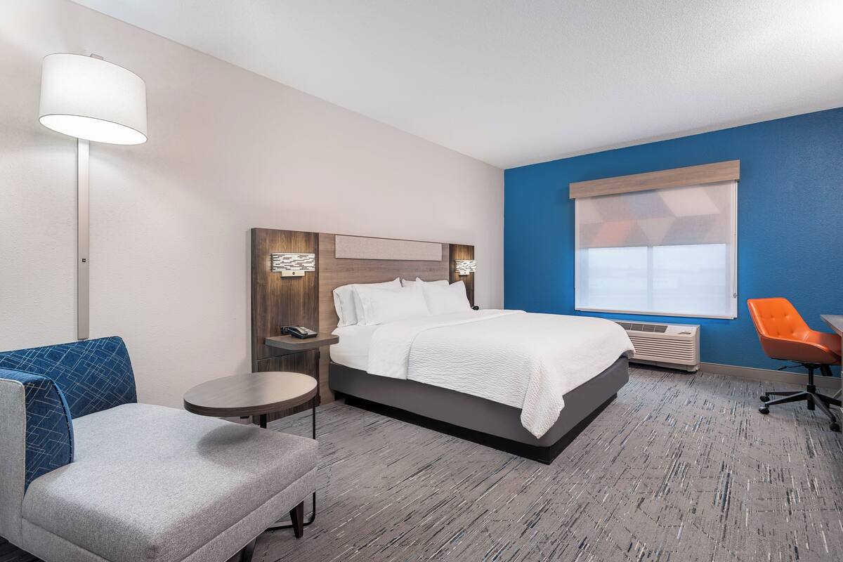 A hotel room with a bed, a desk, a chair, a lamp, and a window.