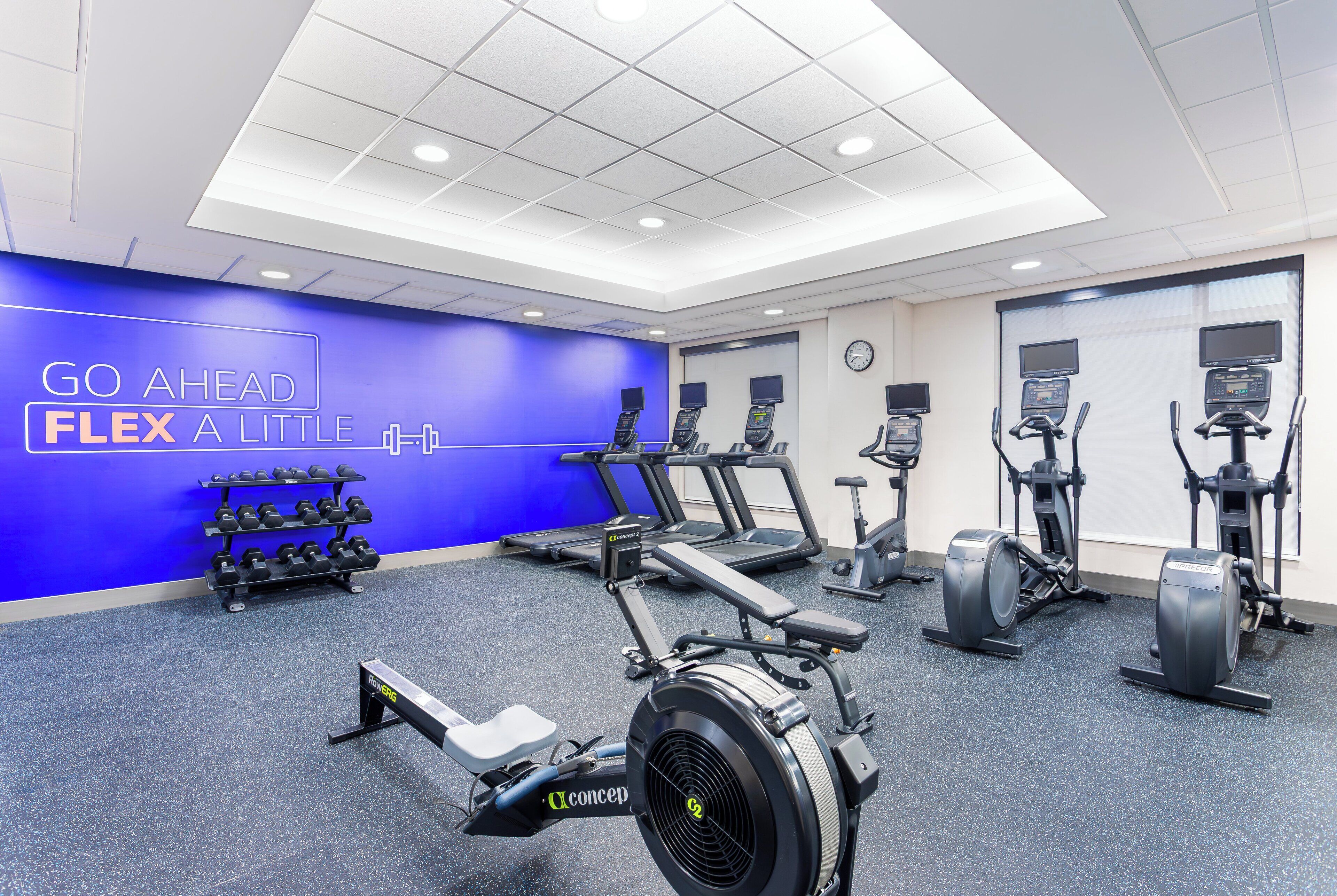 A gym with cardio machines, dumbbells, and a motivational wall.