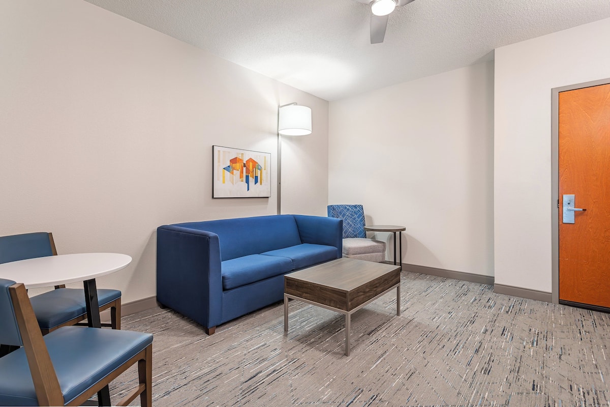 A room with a blue sofa, a small round table, and two chairs. There is a door on the right and a wall-mounted lamp.
