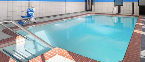 An indoor swimming pool with a tiled floor, a pool ladder, and a blue wall.