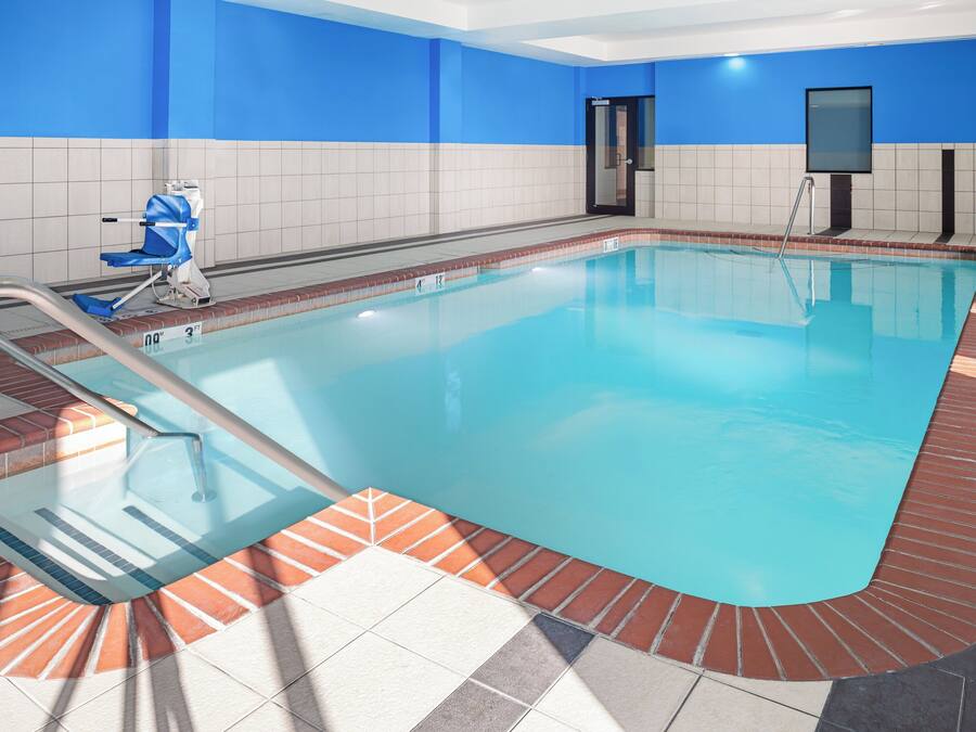 An indoor swimming pool with a tiled floor, a pool ladder, and a blue wall.