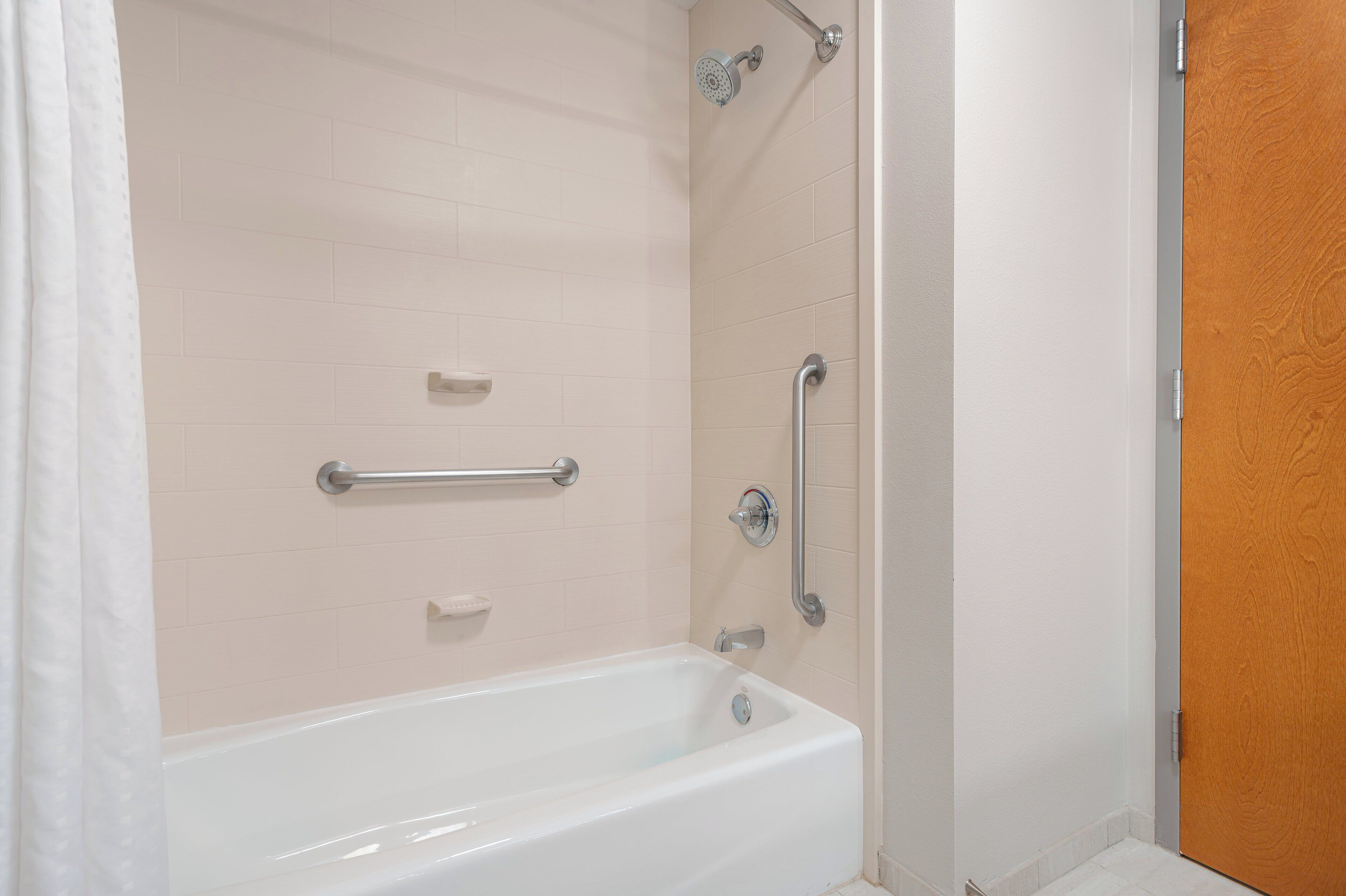 A bathroom with a bathtub, a shower with a handheld showerhead, and a door with a wooden panel.