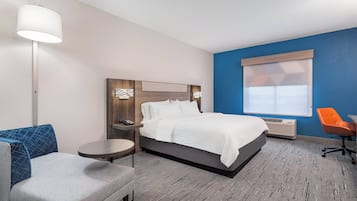 A hotel room with a bed, a desk, a chair, a lamp, and a window.