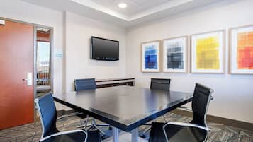 A conference room with a long table, four chairs, a flat-screen TV, and three framed artworks on the wall.
