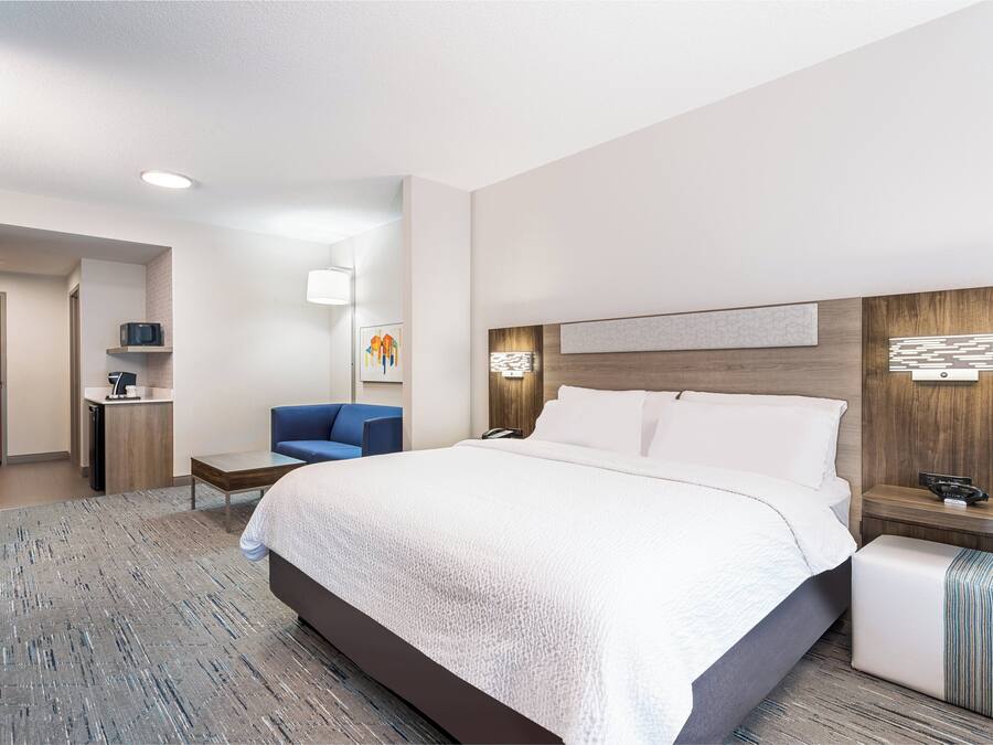 Quarto de hotel com uma cama grande, uma escrivaninha com cadeira, uma kitchenette pequena e um banheiro.