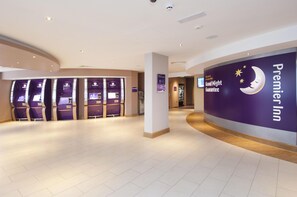 A hotel lobby with a curved reception desk, a 'Good Night Guarantee' sign, and multiple self-service kiosks. - Premier Inn Heathrow Airport Terminal 5 (West Drayton)